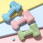 Three textured dumbbell-shaped toys in blue, pink, and green on a colorful background.